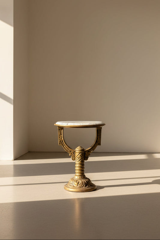 Small round table with marble top and gold decorative base on a dark floor.