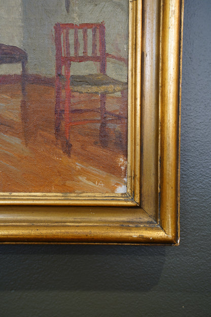 Close-up of a framed painting showing part of a red chair in a room with a warm brown floor, mounted on a dark textured wall.
